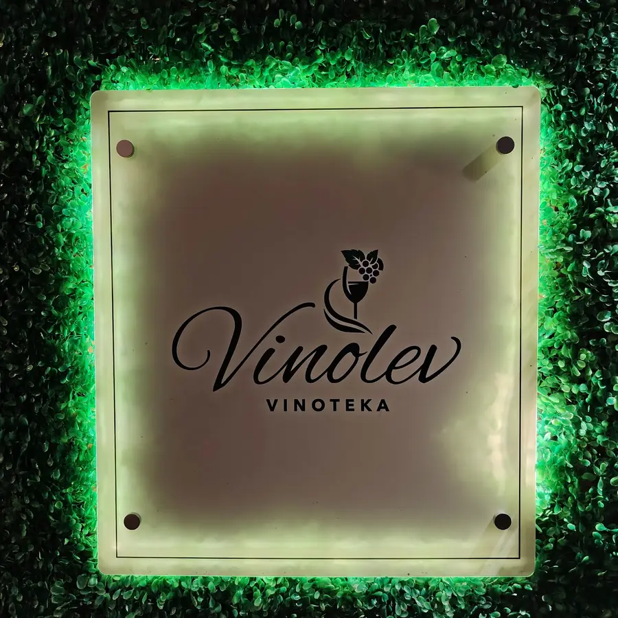 Natpis Vinolev vinoteka na zidu od zelenila, uokviren zelenim svetlom